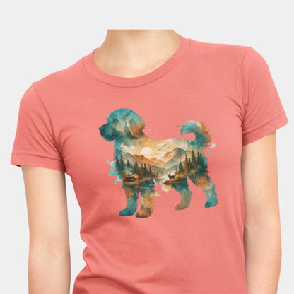 A woman wearing a coral silk colored short-sleeve crewneck t-shirt featuring a watercolor-style graphic of a goldendoodle dog silhouette filled with a scenic landscape of mountains, trees, and a lake.