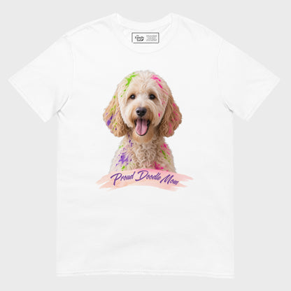 A white short-sleeve crewneck t-shirt featuring a graphic print of a goldendoodle dog with colorful paint on its fur and a banner reading 'Proud Doodle Mom'.