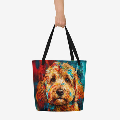 A tote bag with black handles featuring a colorful, textured painting of a goldendoodle's face, held by a hand against a light gray background.