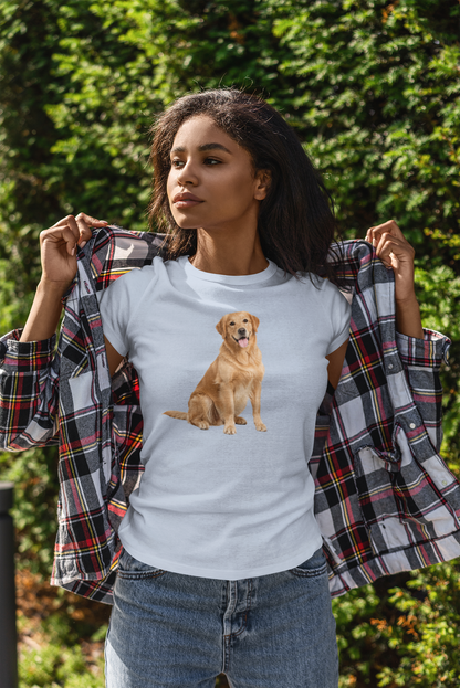 A woman outdoors wearing a light blue t-shirt with a graphic of a golden retriever dog, holding open a plaid flannel shirt over her shoulders. She is wearing blue jeans, with a background of green foliage.