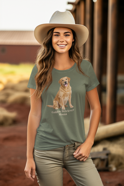 A woman wearing a military green graphic t-shirt with a golden retriever print and the text 'Golden Retriever Mama', paired with a light beige cowboy hat and khaki pants, standing in front of a rustic wooden barn.