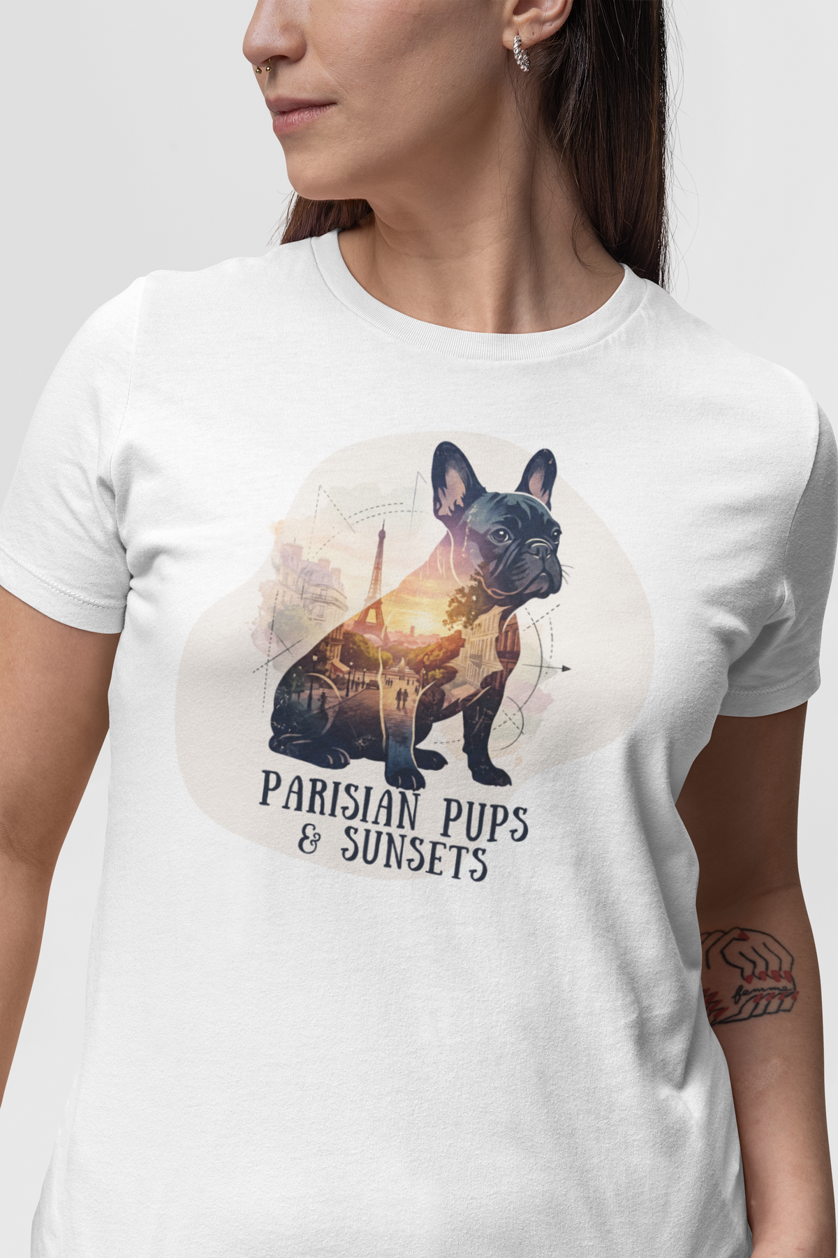 A woman wearing a white short-sleeve crewneck t-shirt with a graphic print of a French Bulldog in Paris with the text 'PARISIAN PUPS & SUNSETS'.