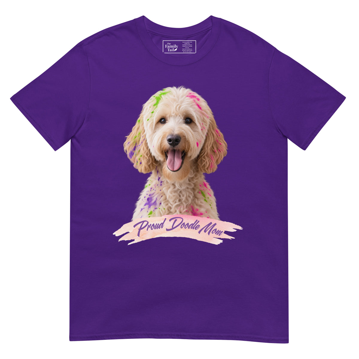 A purple short-sleeve crewneck t-shirt featuring a graphic print of a goldendoodle dog with colorful paint on its fur and a banner reading 'Proud Doodle Mom'.