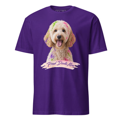 A purple short-sleeve crewneck t-shirt featuring a graphic print of a goldendoodle dog with colorful paint on its fur and a banner reading 'Proud Doodle Mom'.